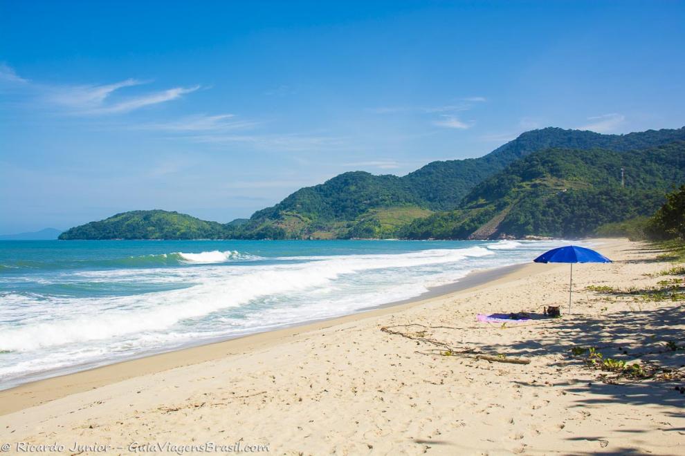 Imagem de uma guarda sol azul nas areias e o lindo mar da Praia do Puruba.